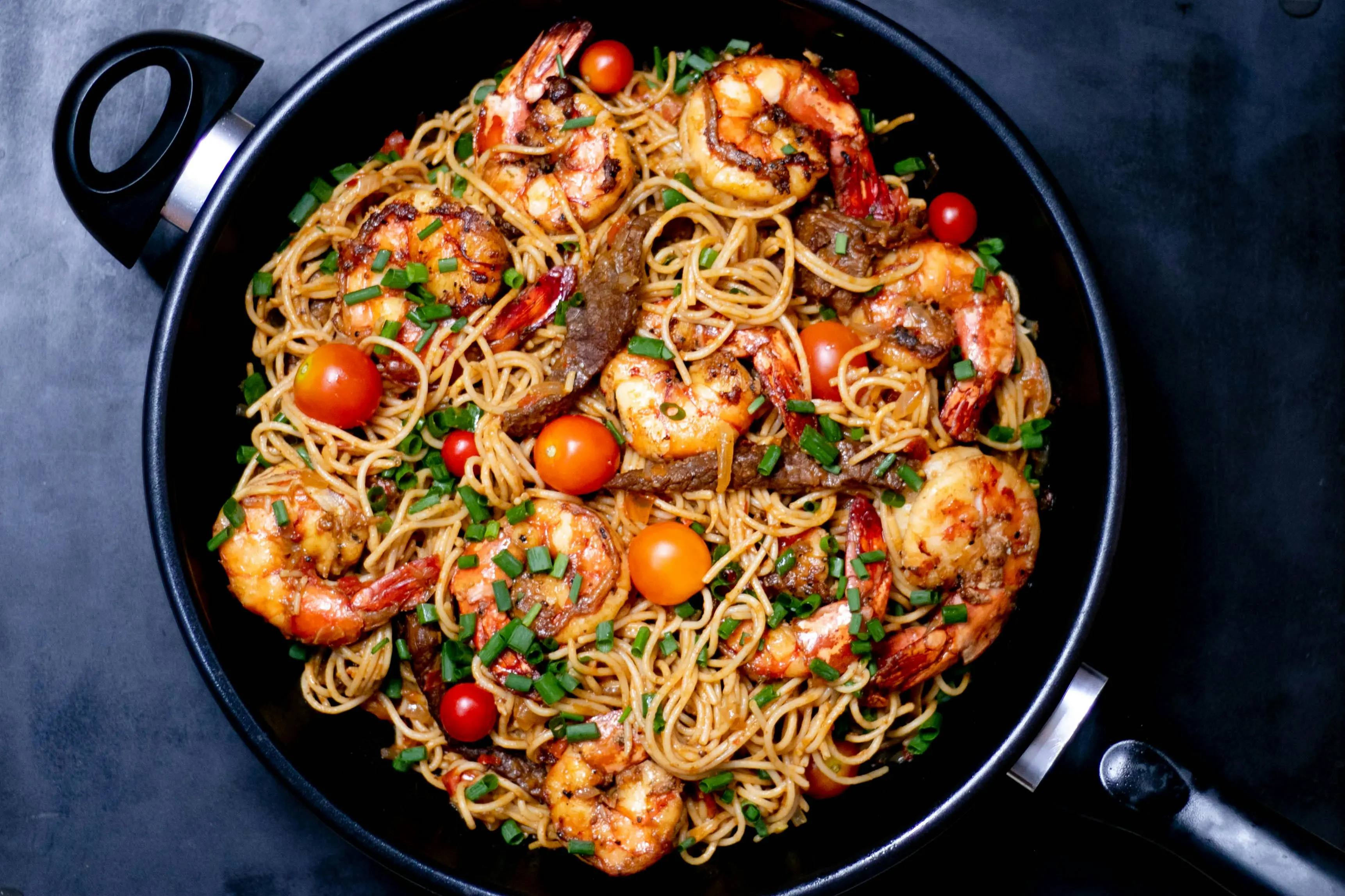 Pan of shrimp pasta with cherry tomatoes and chives